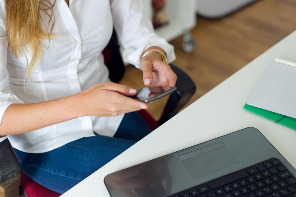 Eine Frau, die ein Smartphone in den Händen hält und an einem Tisch sitzt. 